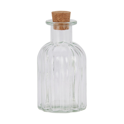 A clear, ribbed glass bottle with a bulbous shape and a cork stopper. The bottle is empty, standing upright against a plain white background.