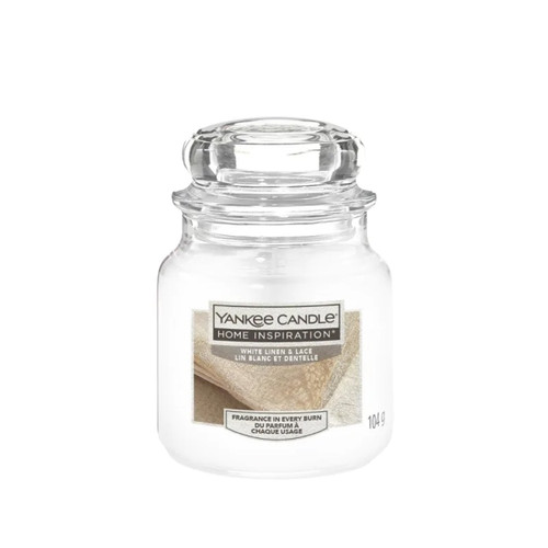 A glass jar candle labeled "Yankee Candle Home Inspiration," featuring a "White Linen & Lace" scent. The jar is transparent with a subtle, elegant design.