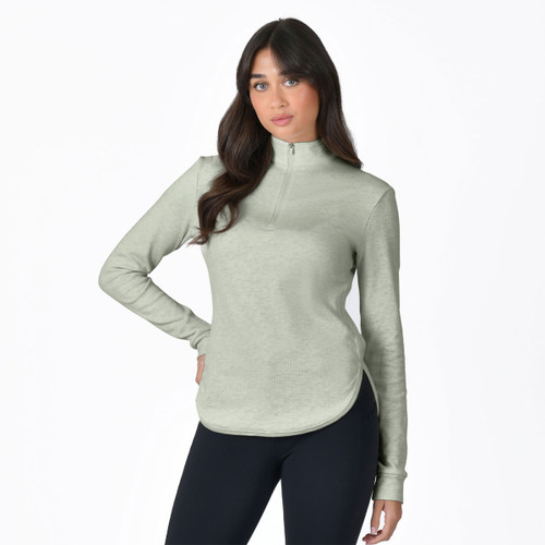 Woman wearing a light sage green long-sleeve quarter zip fleece top with curved hem, styled with black leggings.