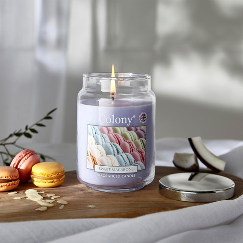 Colony Sweet Macarons fragranced candle burning on a wooden surface with pastel macarons beside it, creating a cosy, dessert-inspired atmosphere.