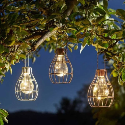 Hanging from a tree branch are three cage lantern lights glowing warmly against a dusky sky, surrounded by green leaves, creating a cosy ambiance.