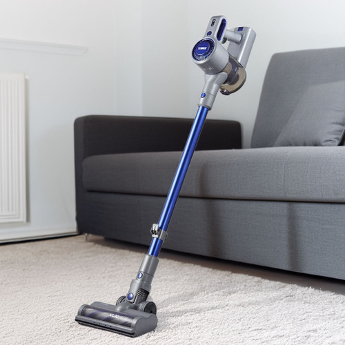 A sleek, cordless vacuum cleaner with a blue and gray design stands on a light-coloured carpet near a modern gray sofa, conveying a clean, tidy home feel.