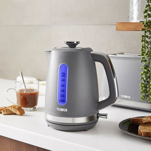 A sleek grey electric kettle with a blue water level indicator sits on a kitchen counter. Nearby, there's a glass cup of coffee and slices of toast, creating a cosy kitchen scene.