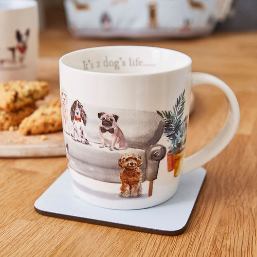 White ceramic mug with illustrated dogs sitting on a grey sofa, shown on a wooden table with biscuits in the background.