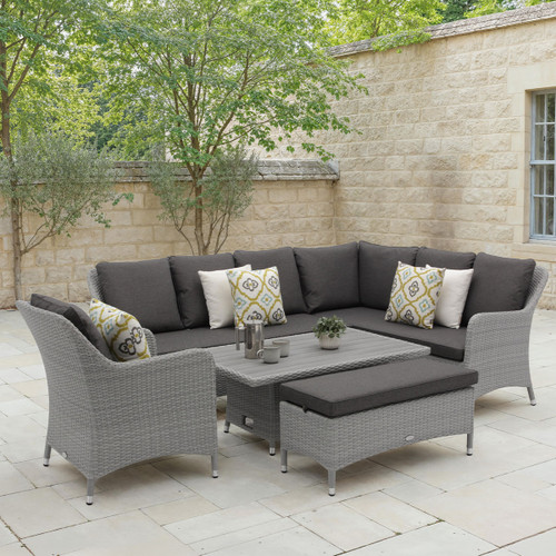 A modern outdoor lounge set with cushioned seating, decorative pillows, and a coffee table, surrounded by greenery and a stone wall backdrop.