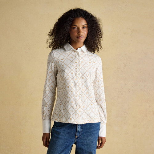 A woman wearing a cream equestrian-print long-sleeve shirt paired with blue jeans, standing against a neutral backdrop.