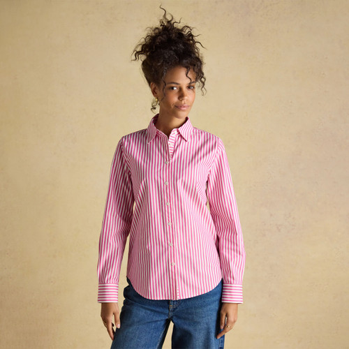 A woman wearing a long-sleeved pink and white striped shirt with a classic collar and button front, paired with blue jeans against a neutral background.