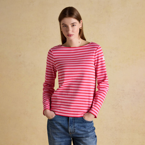 A woman wearing a pink long-sleeve Breton top with bold red horizontal stripes, styled with relaxed blue jeans.