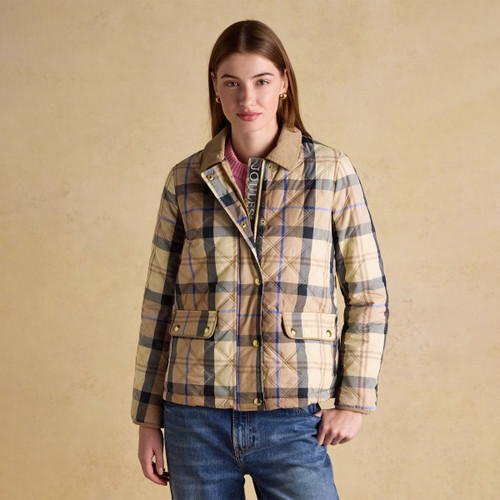 A woman wearing a beige checked quilted jacket with gold poppers and patch pockets, styled with blue jeans against a neutral backdrop.