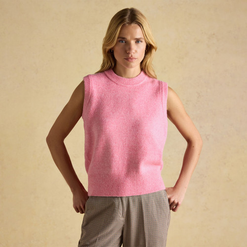 Woman wearing a bright pink sleeveless knitted vest with a ribbed neckline and hem, styled with checked trousers against a soft beige background.