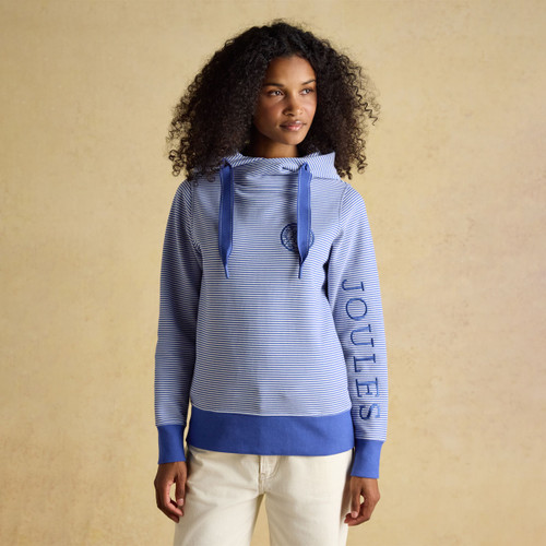 Women’s blue and white striped hoodie with wide drawstrings, relaxed fit and embroidered chest emblem, worn with cream trousers.