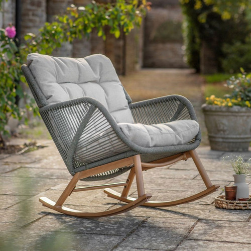 Fern green rope-woven rocking lounge chair with a light coloured cushion, shown on a stone patio in a garden.