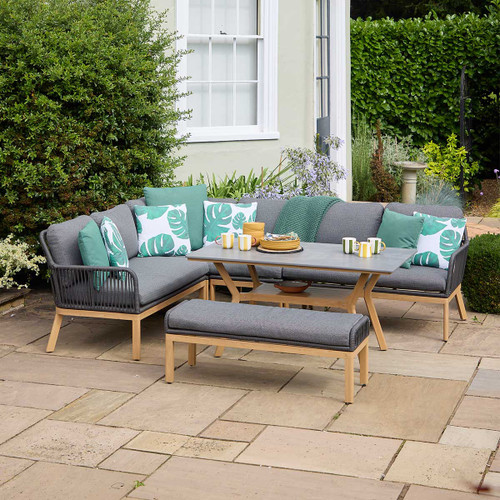 A view of an LG Outdoor Peru 8 Seater modular dining garden furniture set with a wood effect and grey cushions on a patio next to a house