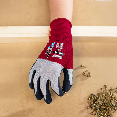 A red and grey work glove with "Wonder Grip" text holds a small screw over a table scattered with screws, conveying a sense of construction work.