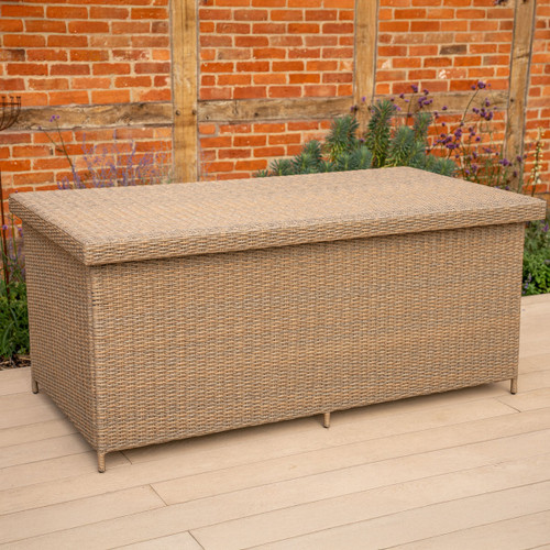 Large rectangular outdoor rattan storage box with a flat woven lid, shown on a light decking area in a garden setting.