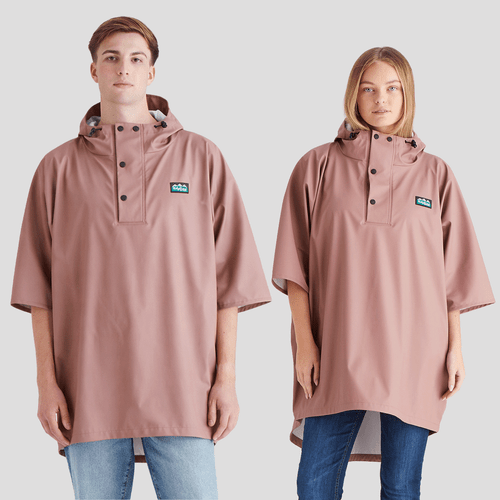 Dusty pink waterproof poncho with a hood, black button placket, wide sleeves, and a small chest logo patch, shown on two models.