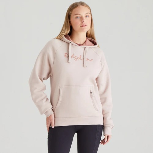 Front view of a woman wearing a light pink pullover hoodie with drawstrings and “Ridgeline” logo text across the chest. The hoodie features a large front kangaroo pocket with a vertical zip detail. She pairs it with black leggings against a plain light grey background.