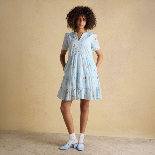 Woman wearing a light blue striped short-sleeve dress with floral print, V-neckline and tiered skirt, styled with white socks and blue Mary Jane shoes.