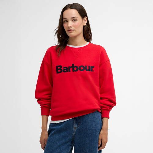 Model wearing a red Barbour crew-neck sweatshirt with large navy logo, styled with blue jeans.