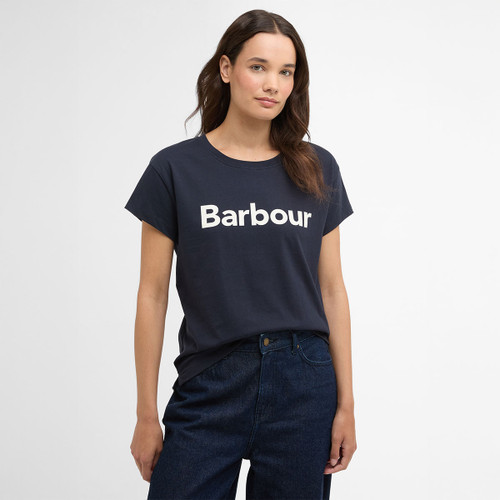 Model wearing a navy Barbour short-sleeve T-shirt with large white logo print, styled with dark blue jeans.