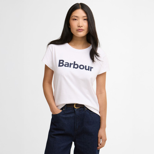 Model wearing a white Barbour logo T-shirt with navy lettering, styled with dark denim jeans.