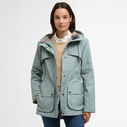 Model wearing a pale blue Barbour hooded waterproof jacket with popper fastening and large front patch pockets.