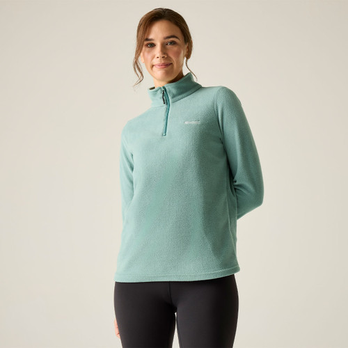 Front view of a model wearing an ivy green half-zip fleece with a high neck, styled with black leggings.