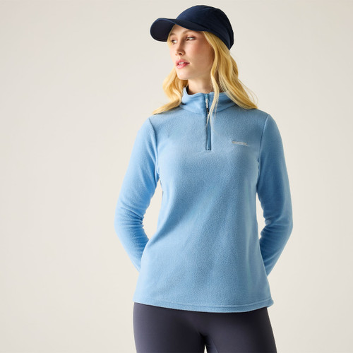 Model wearing a washed denim blue women’s half-zip fleece with a high collar, shown from the front.