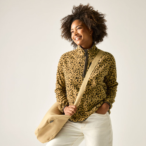 Model wearing a tan leopard print fleece with high collar and half-zip, styled with cream trousers and a beige crossbody bag.