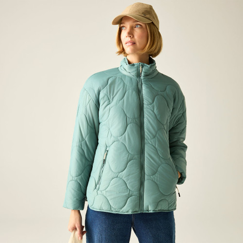 Model wearing a green quilted jacket with a high stand collar and zip-through front, styled with a beige cap and blue jeans.