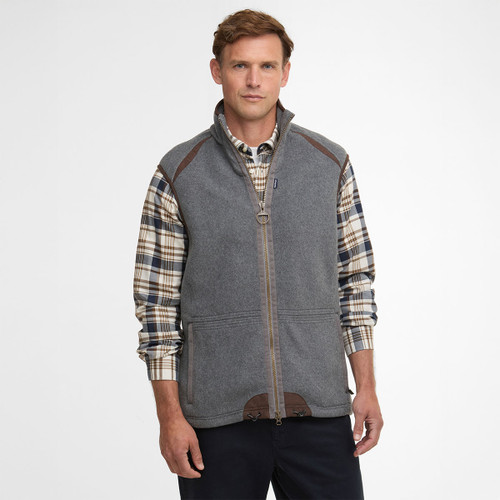 Man wearing a grey zip-up vest over a plaid shirt, standing against a plain white background. He has a neutral expression and casual pose.