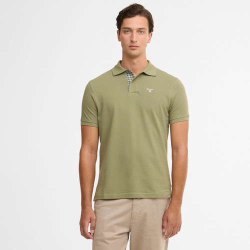 A man wearing an olive-green polo shirt with a subtle logo stands against a plain white background. He has a neutral expression, and wears khaki pants.