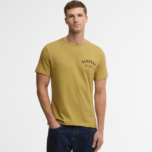 A man in a mustard yellow T-shirt with "Barbour Est. 1894" on the chest, stands casually with one hand in his pocket. He wears dark jeans against a plain white background.