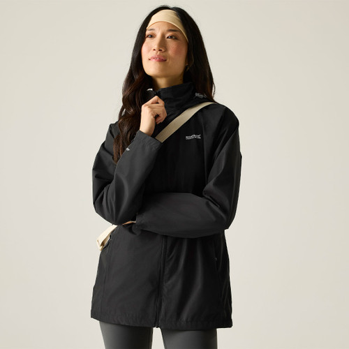 Woman wearing a black hooded waterproof jacket, zipped up, with a high collar and a neutral crossbody strap.