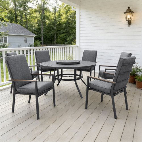 Cosy outdoor patio with a round table and five padded grey chairs on a wooden deck. Surrounded by white railings and a lush green garden.