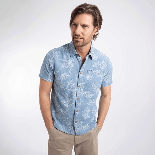 Man wearing a light blue short-sleeve chambray shirt with a white leaf print and button fastening, paired with beige shorts