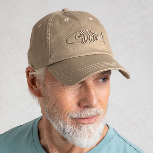 Model wearing stone-coloured twill cap with embroidered fish skeleton logo, looking to the side.