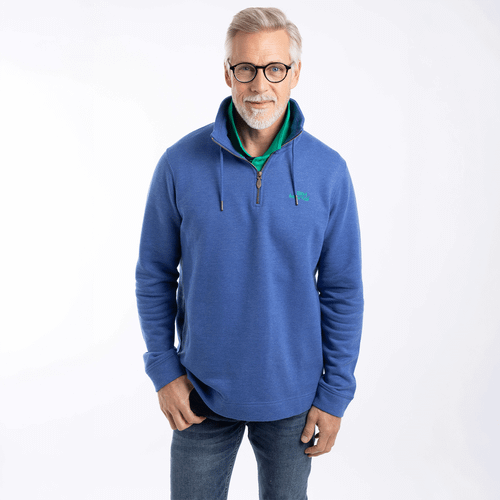 Man wearing a blue quarter-zip sweatshirt with drawstring collar and small chest logo, layered over a green polo shirt and paired with jeans.