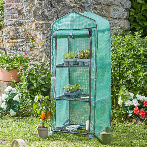 Small green mesh walk-in mini greenhouse with three shelves, shown in a garden with seed trays and potted plants.