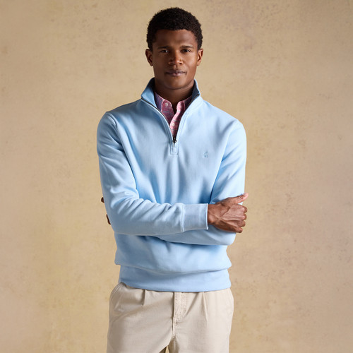 Model wearing a light blue quarter-zip fleece layered over a pink checked shirt, standing with arms crossed against a neutral background.