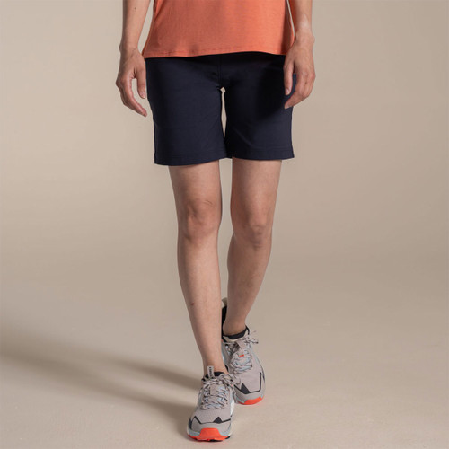 Model wearing navy women’s outdoor shorts with an orange vest and walking trainers, side view.