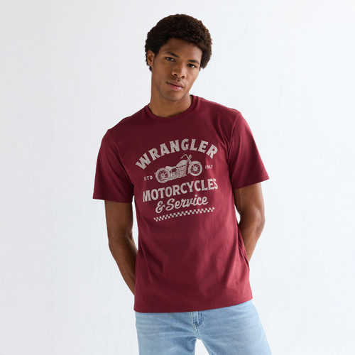 Model wearing a ruby wine Wrangler graphic T-shirt and light blue jeans, front view.
