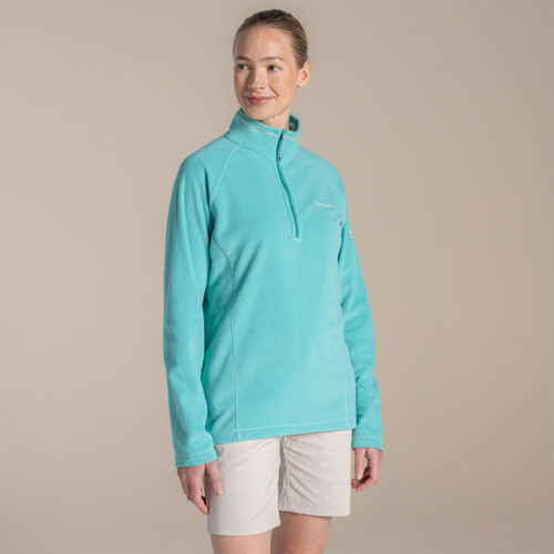 Woman wearing turquoise Craghoppers half-zip fleece with light shorts, angled studio shot.