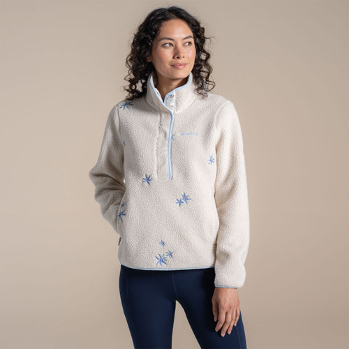 Woman wearing an off-white sherpa fleece pullover with pale blue trim and blue embroidered flowers, three-quarter front view.