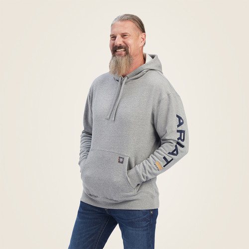 Man wearing a grey Ariat Rebar hoodie with kangaroo pocket and drawstring hood, smiling and standing in a studio setting.