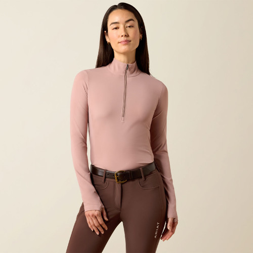 Woman wearing a fitted mauve long-sleeve top with a half-zip, paired with brown riding pants and a belt, exudes a confident and relaxed demeanour.
