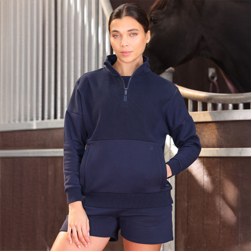 Woman modelling a navy half-zip sweatshirt with high collar and kangaroo pocket, wearing matching shorts in a stable yard.