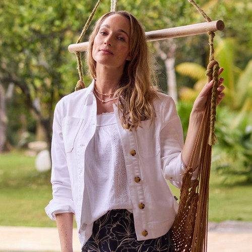 Model wearing a white canvas jacket over a white top, standing outdoors beside a rope swing.