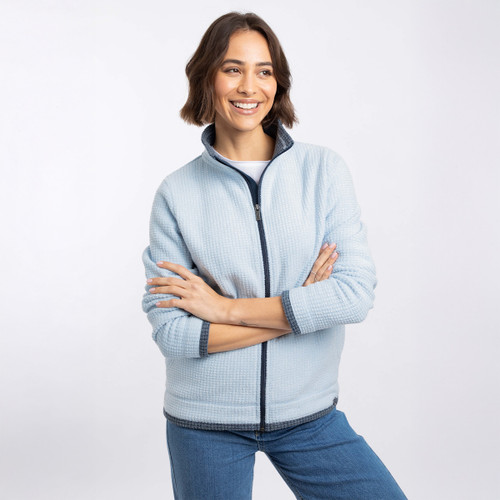 Model wearing a light blue textured zip-up fleece with a stand collar and dark trim, smiling with arms crossed.