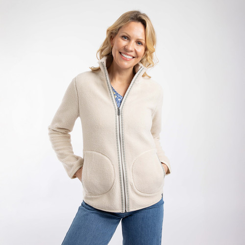 Model wearing an ecru teddy fleece zip-through jacket with a high collar and large curved front patch pockets, hands in pockets.